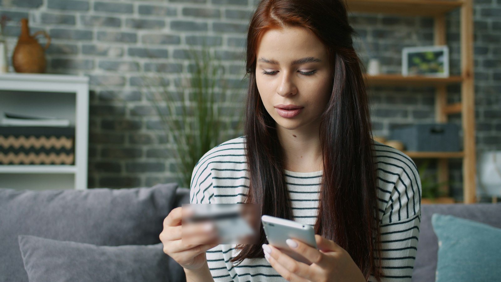 A woman shopping on her phone at home, holding a payment card